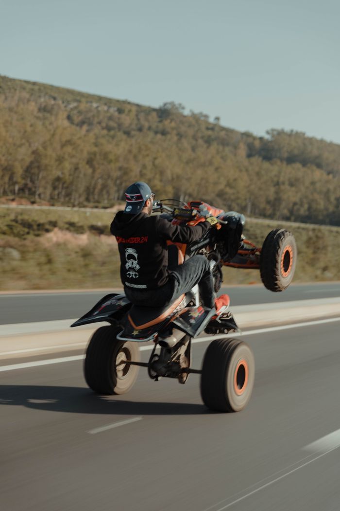 services-03 Man performing exciting wheelie on ATV on a scenic road, showcasing adventure and skill.