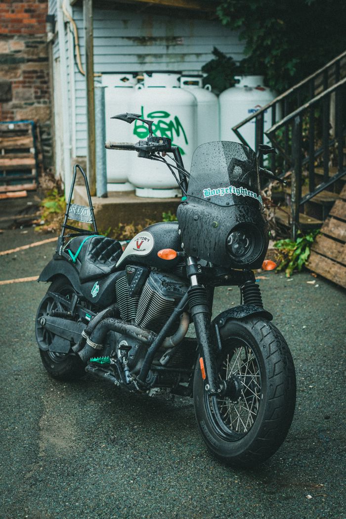 services-01 A sleek black motorcycle with unique decals parked on wet pavement in an urban setting.