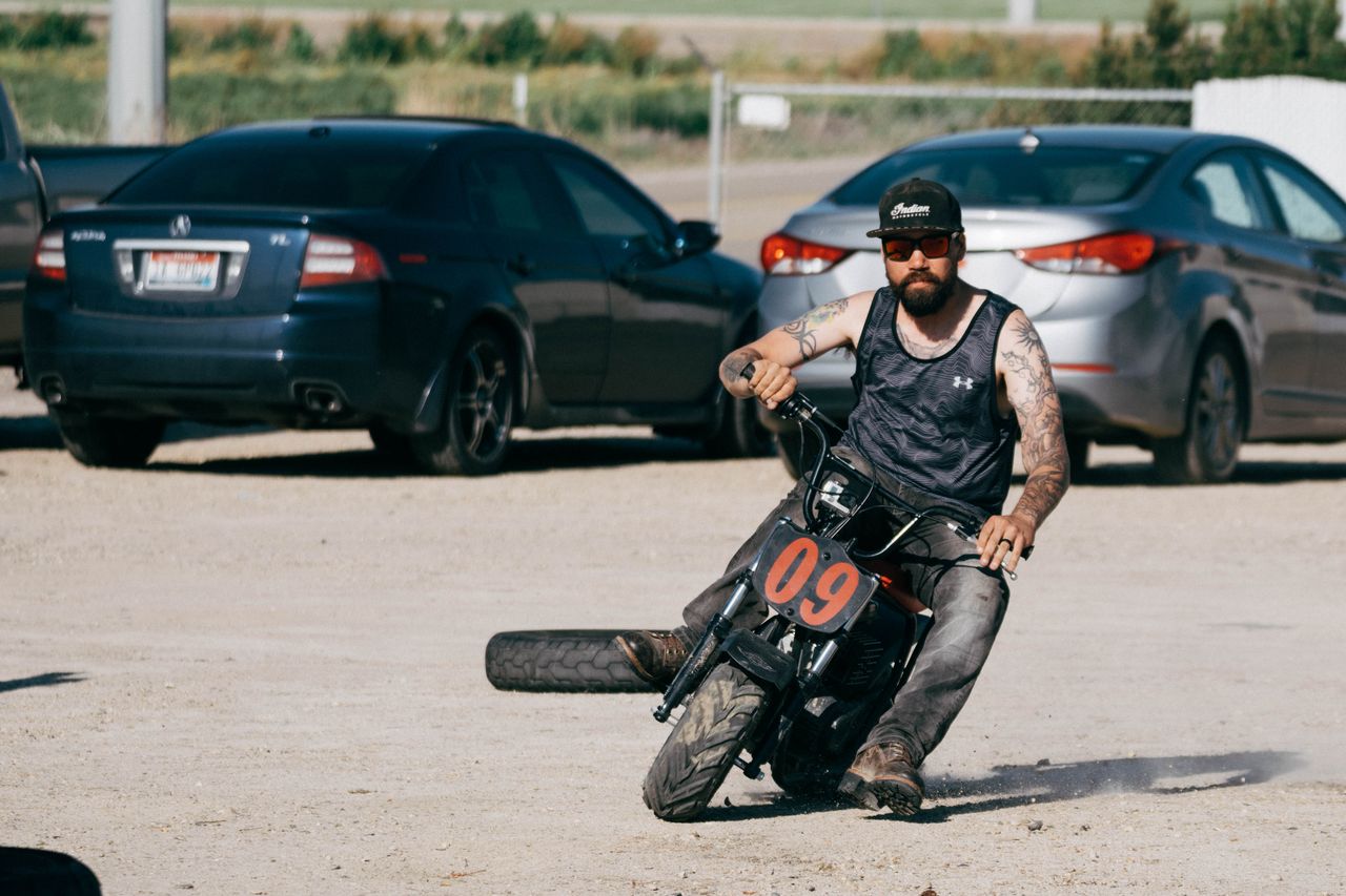Mastering the First Impression: Your intriguing post title goes here A tattooed man riding a small motorcycle performs a stunt in a sunny parking lot.