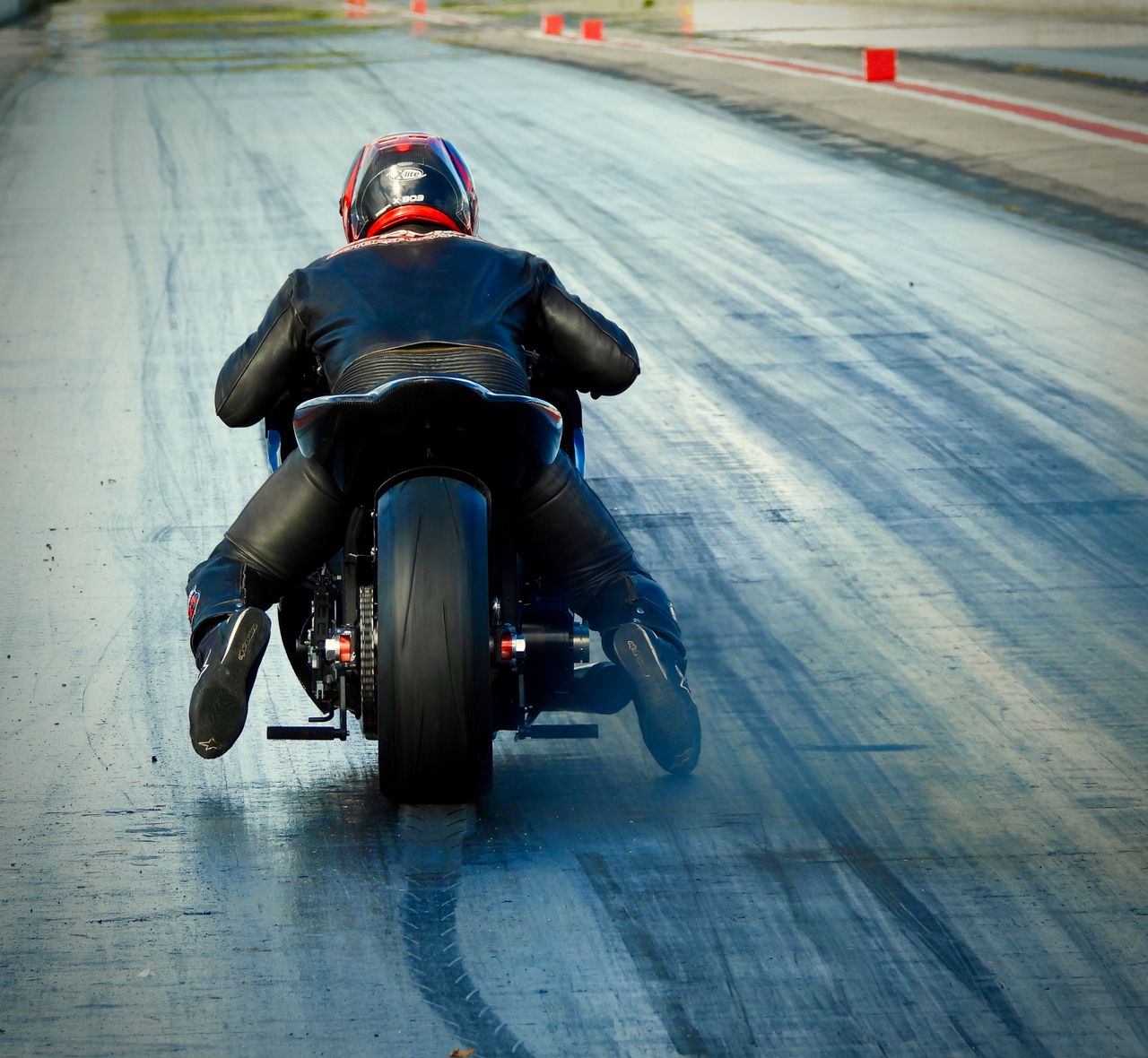 contact-img Back view of a motorcyclist speeding on a race track, showcasing skill and speed.