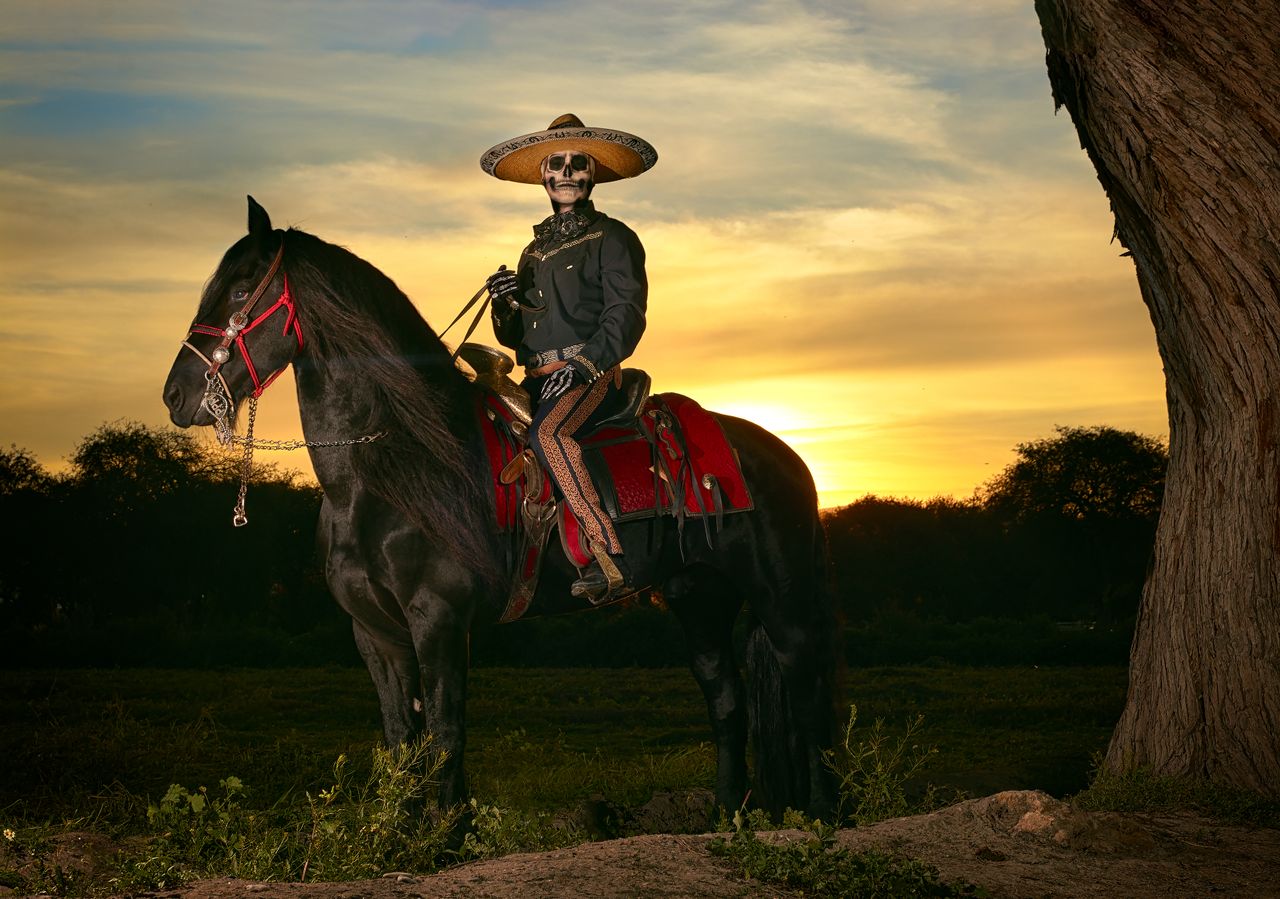services-img A Mexican horseman dressed in a charro outfit rides a black horse during sunset.